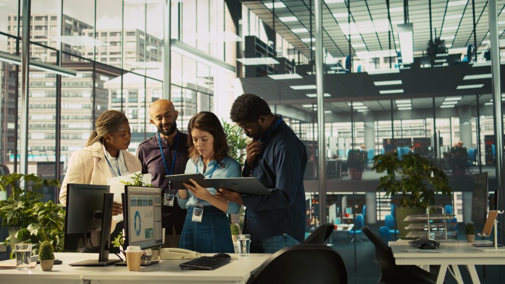 multiethnic coworkers looking over revenue figures on tablet in diverse office